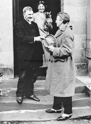 Family photo
John Logie Baird greets his father, the Rev John Baird, and his older sister Annie at the front door of his birthplace, The Lodge in West Argyle Street, in 1928. Annie is holding up her Cairn terrier â€˜Jinkieâ€™ to whom she was devoted. Bairdâ€™s prosperity is reflected in his immaculate attire which includes spats. On the other hand his father has just stepped out of the door and is still wearing his bedroom slippers. 
