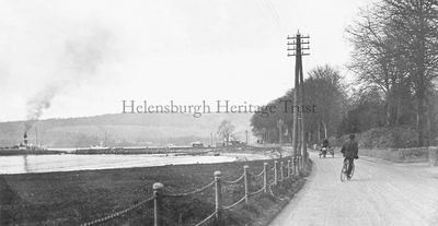 On road to Rhu
A cyclist and a horse and cart make their way along Row (Rhu) road towards Rhu, and a steamer is waiting at the pier in this postcard picture published by M.Gordon of Row Pier. Image date unknown.
